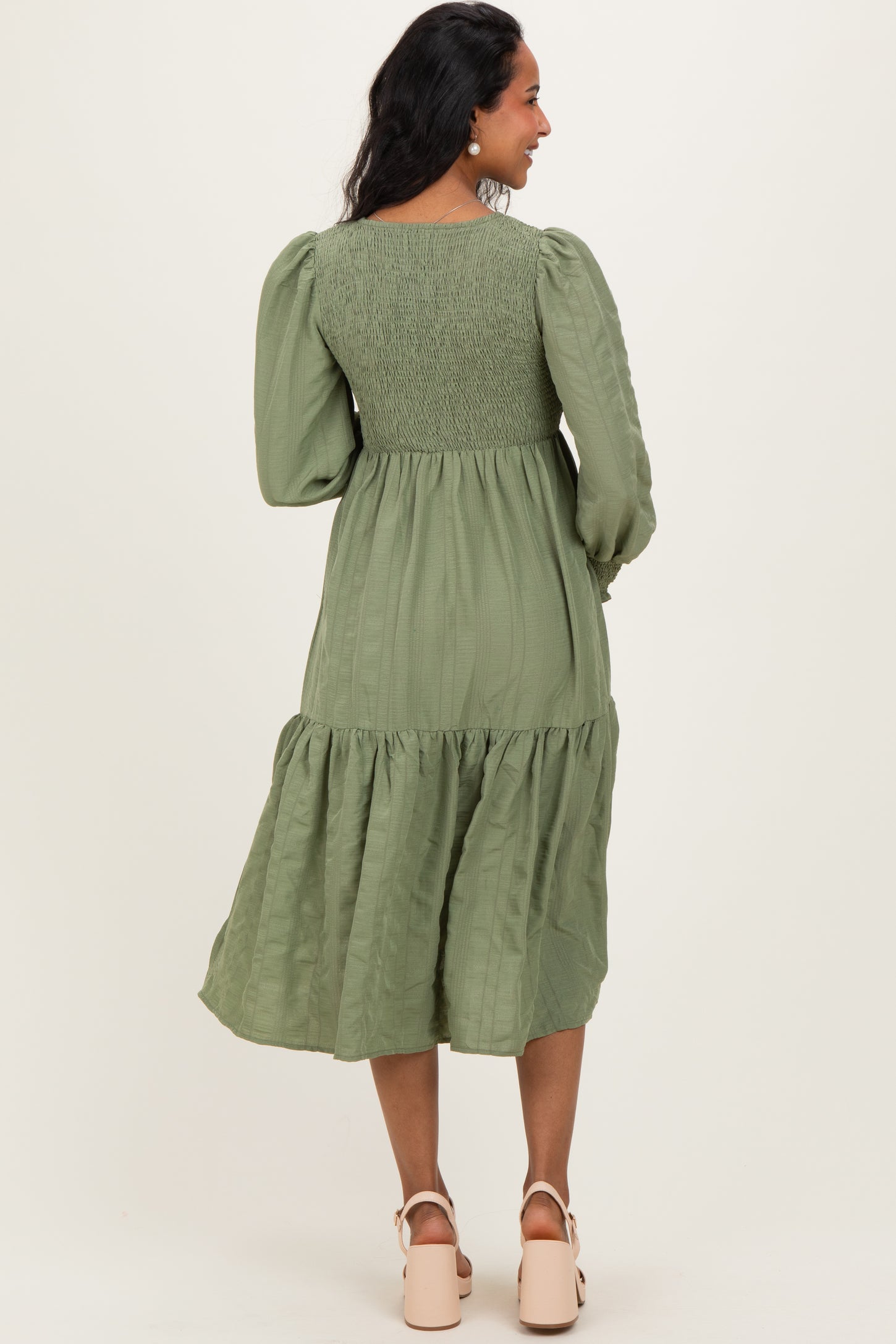 woman wearing an olive green maternity dress with puff sleeves and a tiered skirt, showing a baby bump from the back