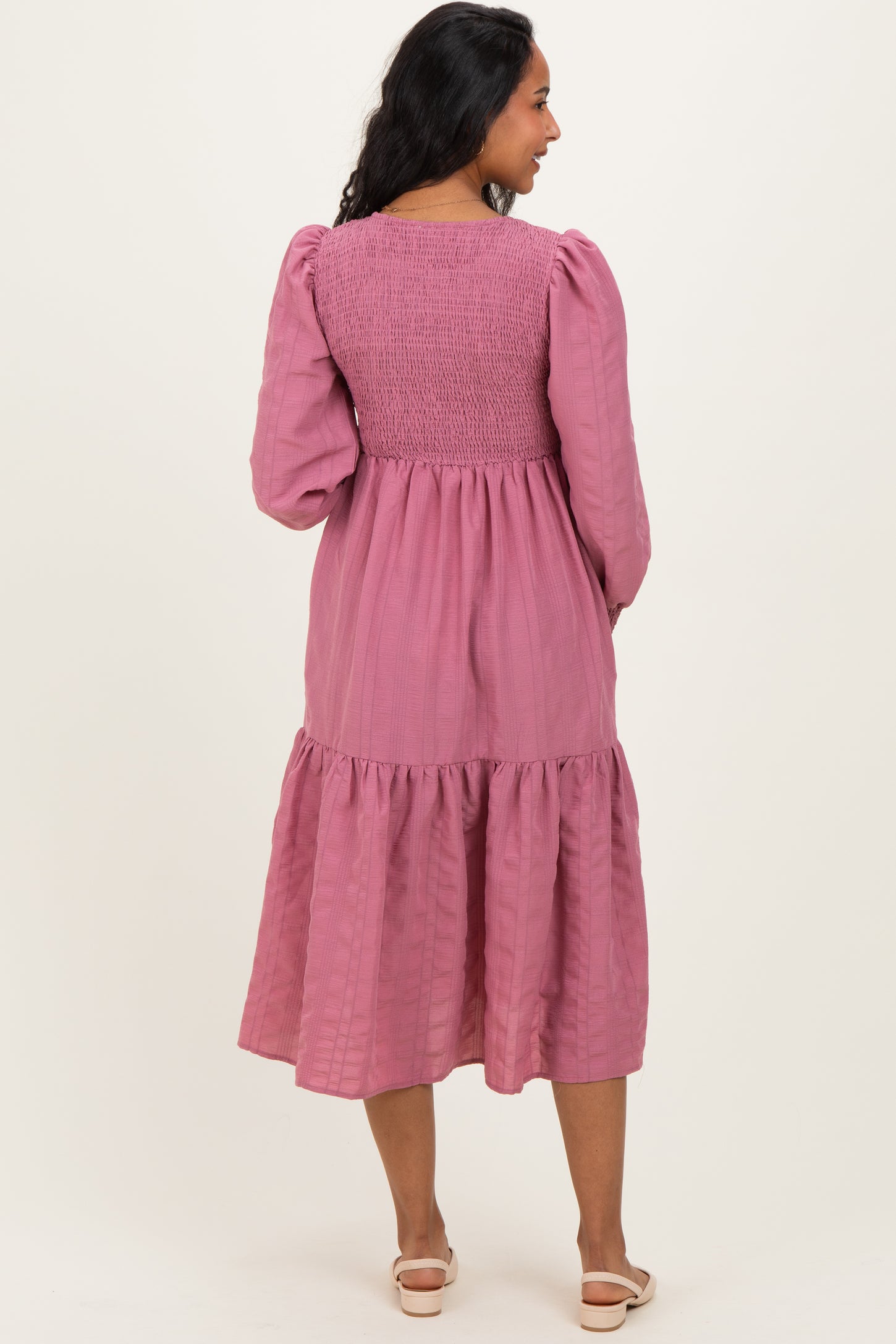 woman wearing a pink maternity dress with smocked bodice and tiered skirt, showing the back view