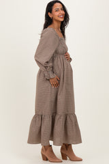 woman wearing a brown gingham long sleeve maternity dress with a tiered skirt and holding her baby bump