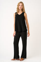 woman wearing a black ribbed sleeveless top and matching wide-leg pants, standing with a relaxed pose