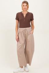 woman wearing a brown short sleeve henley top and light beige wide-leg maternity pants with pockets