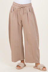 woman wearing light brown wide-leg lounge pants with side pockets and an elastic waist, paired with cozy slippers