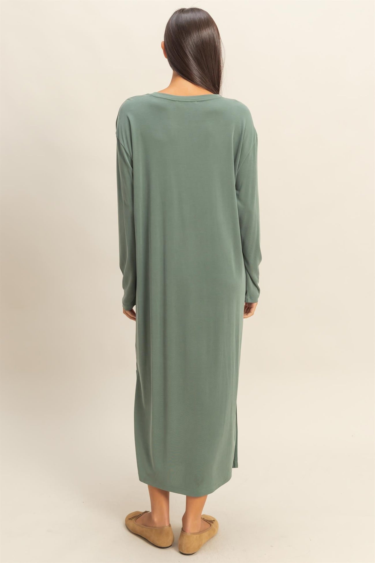 woman wearing a long green oversized dress with long sleeves and side slits, viewed from the back
