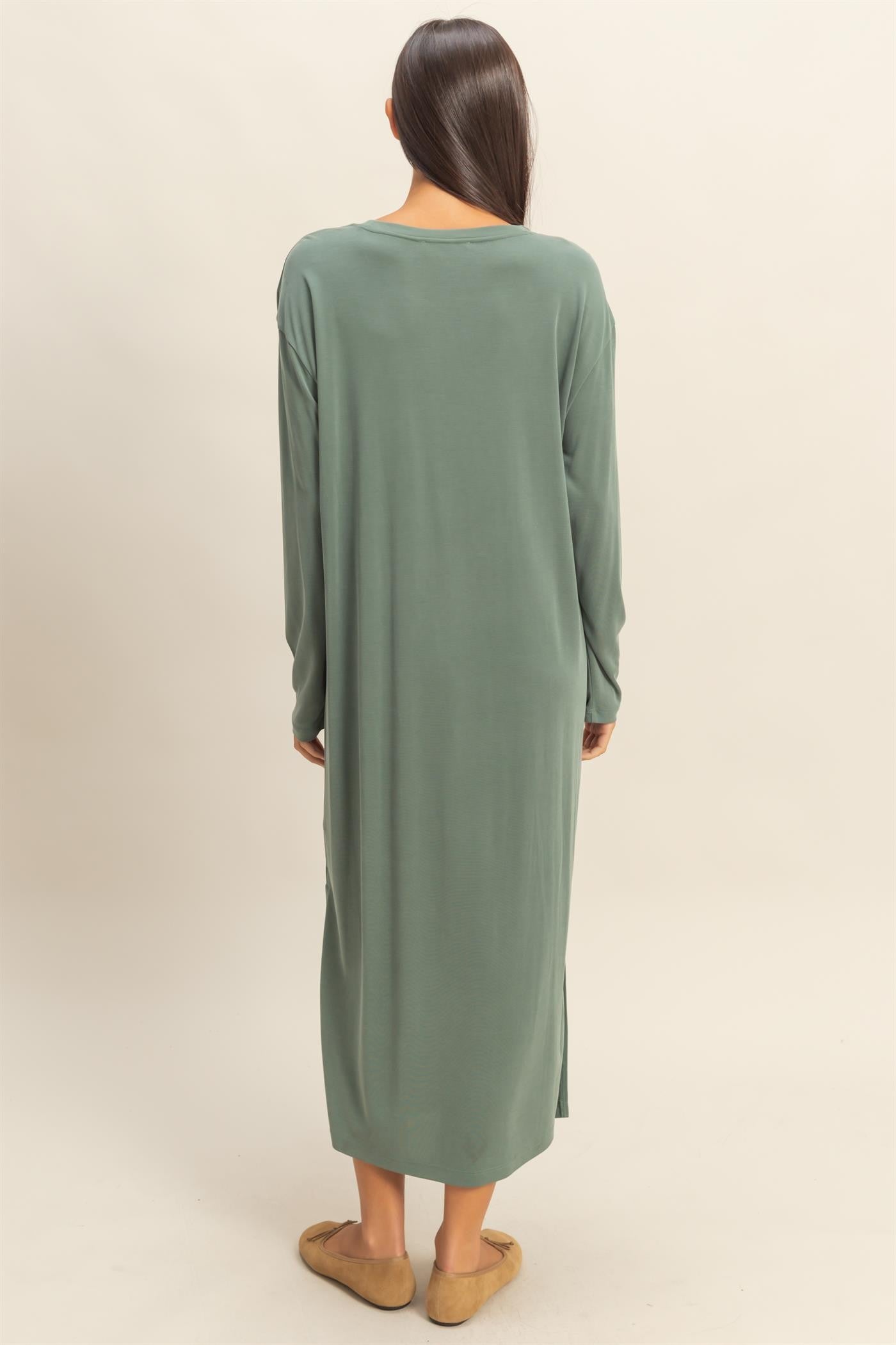 woman wearing a long green oversized dress with long sleeves and side slits, viewed from the back