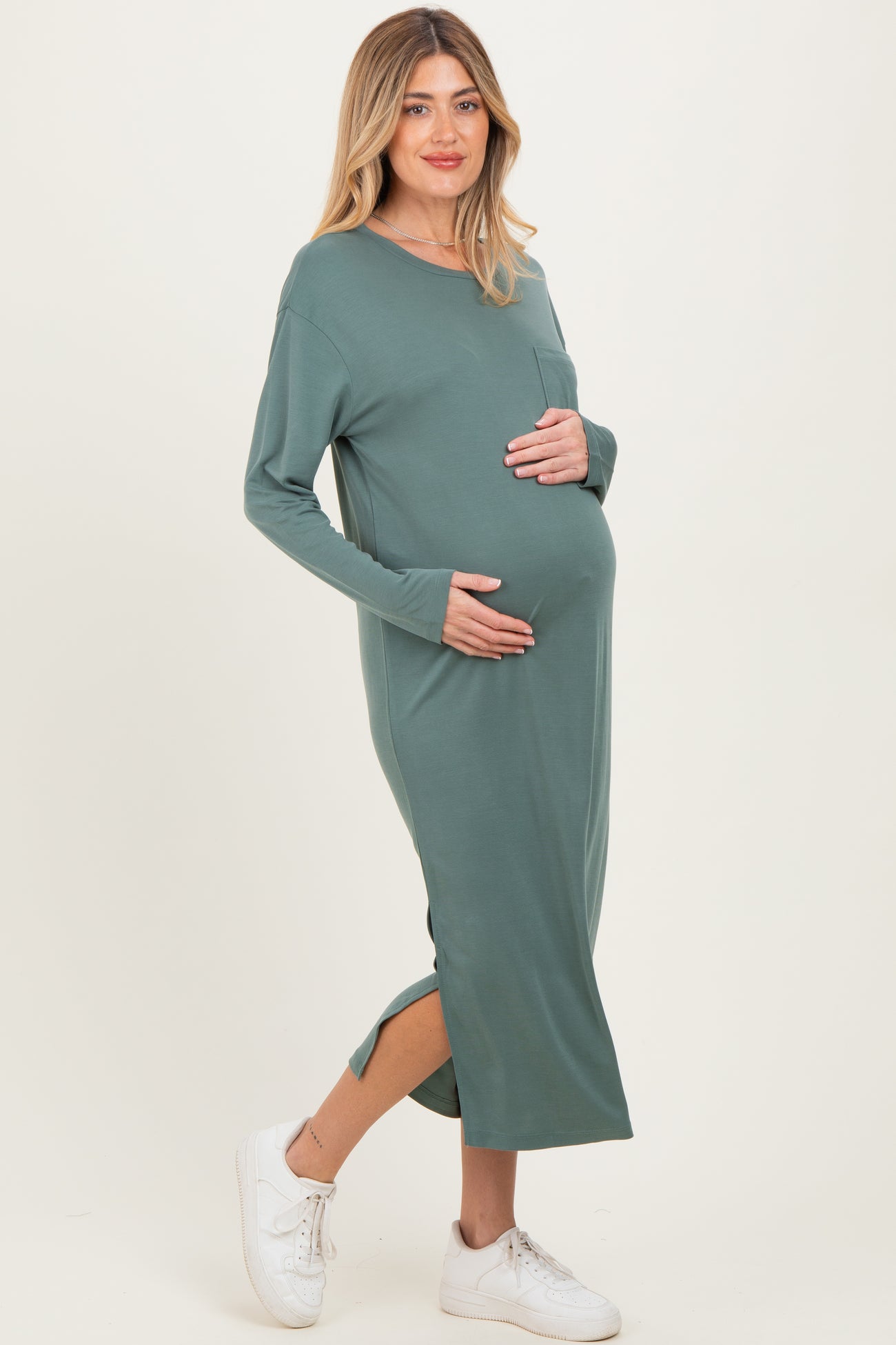 woman wearing a green long sleeve maternity dress with side slits and holding her baby bump