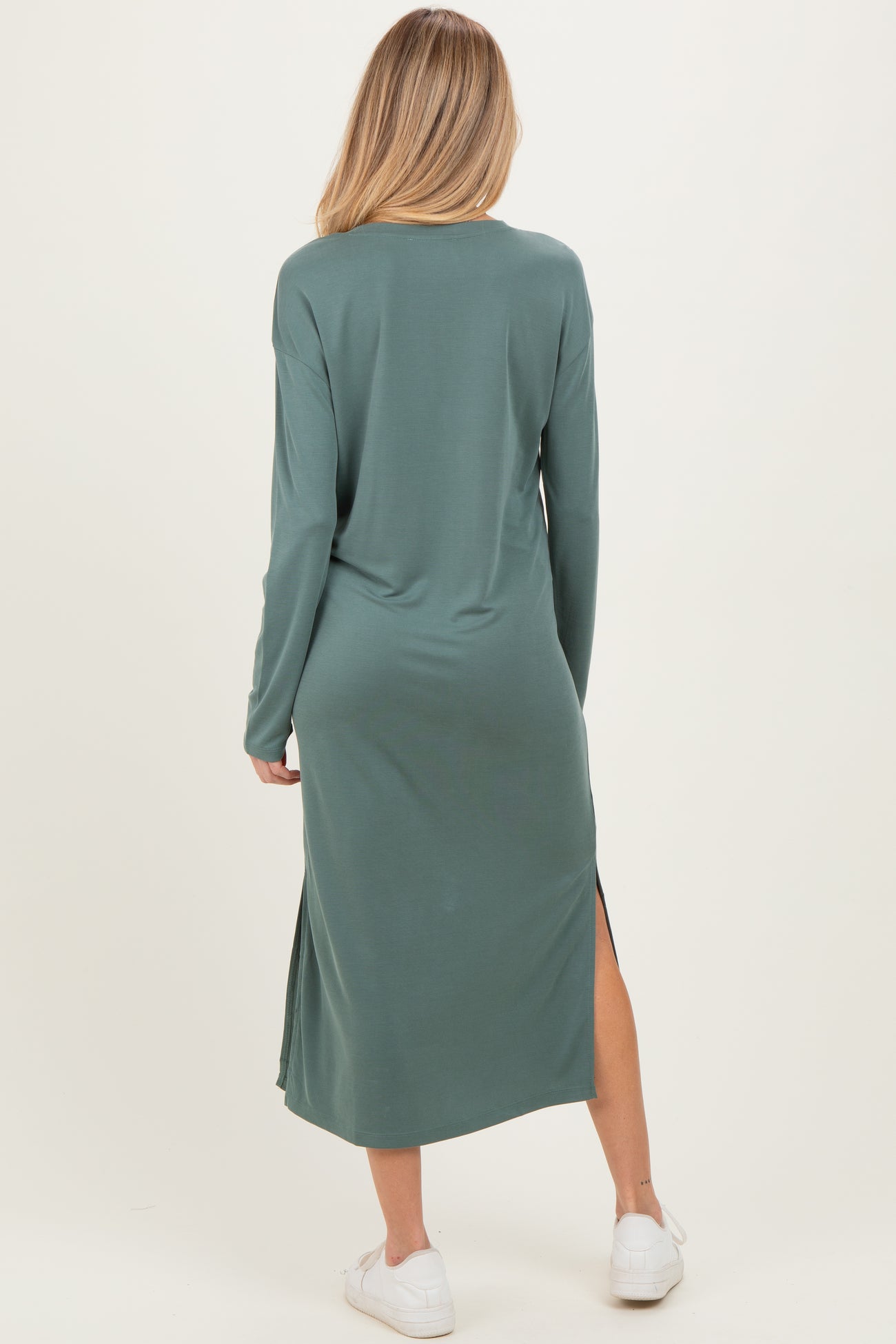 woman wearing a long sleeve green maternity dress with side slits, seen from the back