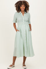 woman wearing a light green maternity dress with a button front and pockets, styled with short sleeves and a smocked bodice