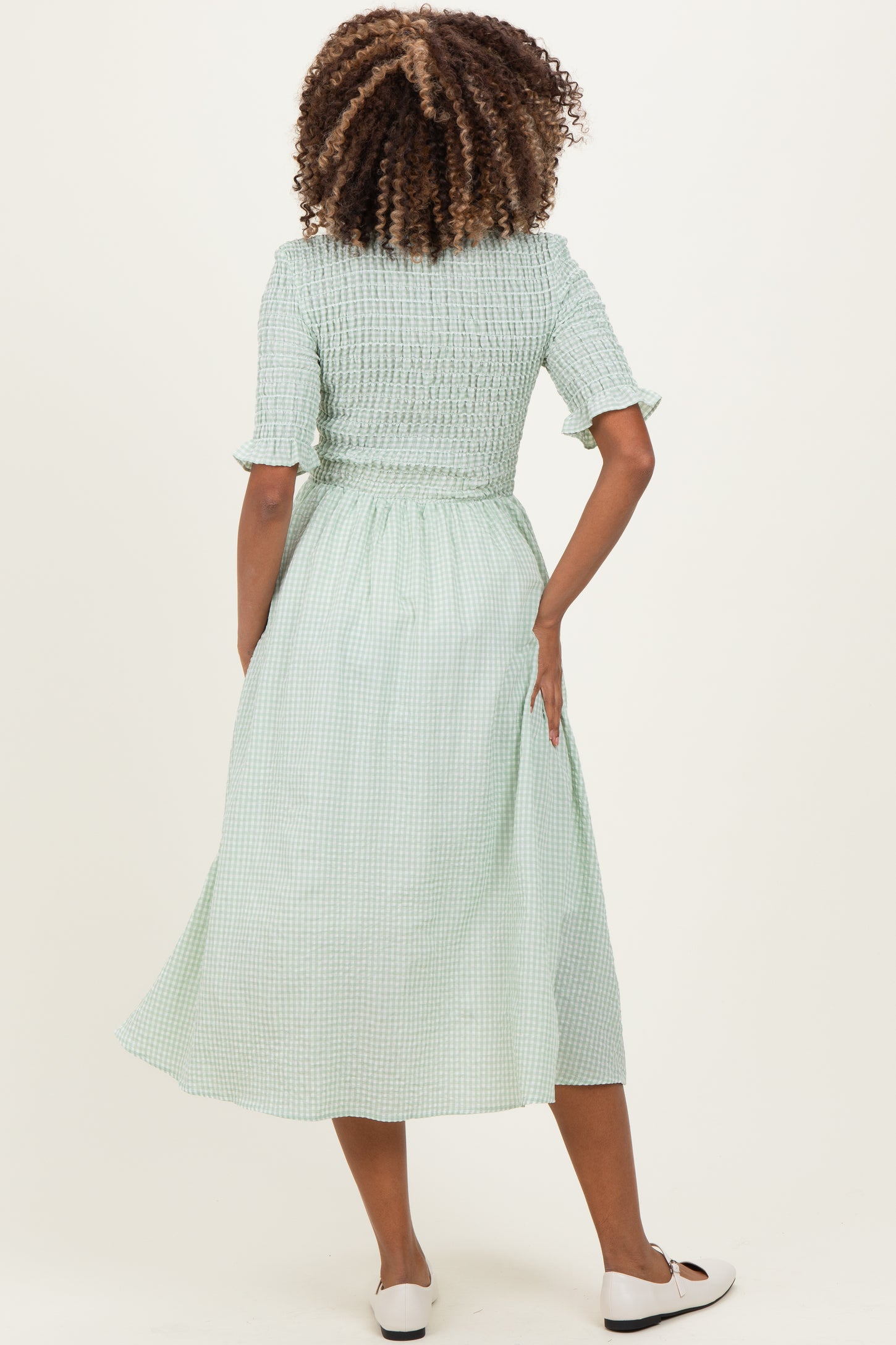 woman wearing a green gingham maternity dress with a smocked bodice and short sleeves, showing a flowing skirt