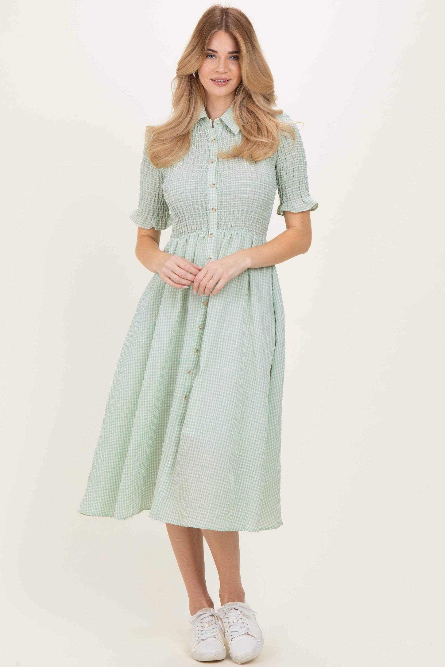woman wearing a green gingham shirt dress with button detail and short sleeves, paired with white sneakers