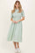 woman wearing a green gingham shirt dress with button detail and short sleeves, paired with white sneakers