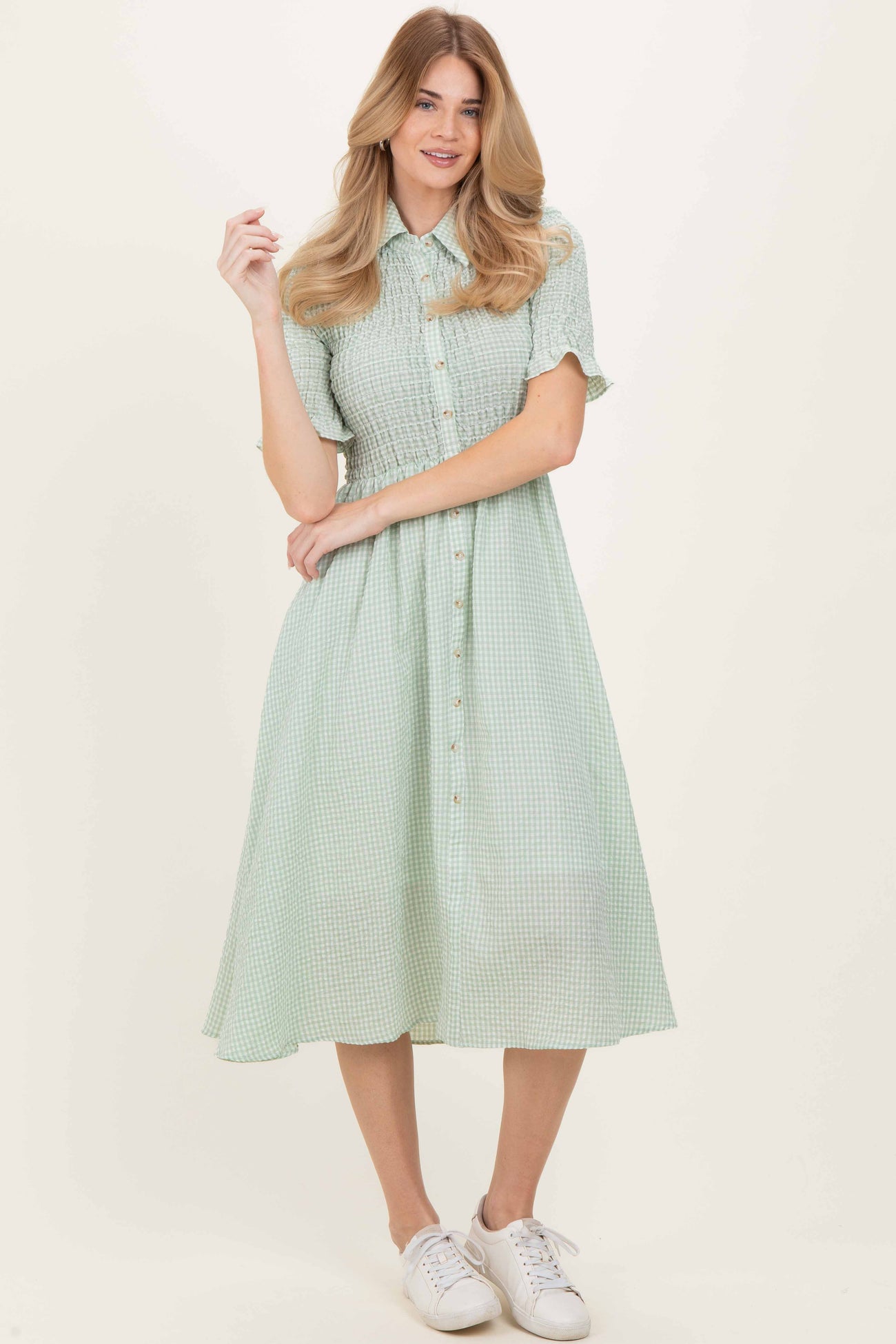woman wearing a green checkered button-up dress with short sleeves and a flared skirt, standing in white sneakers
