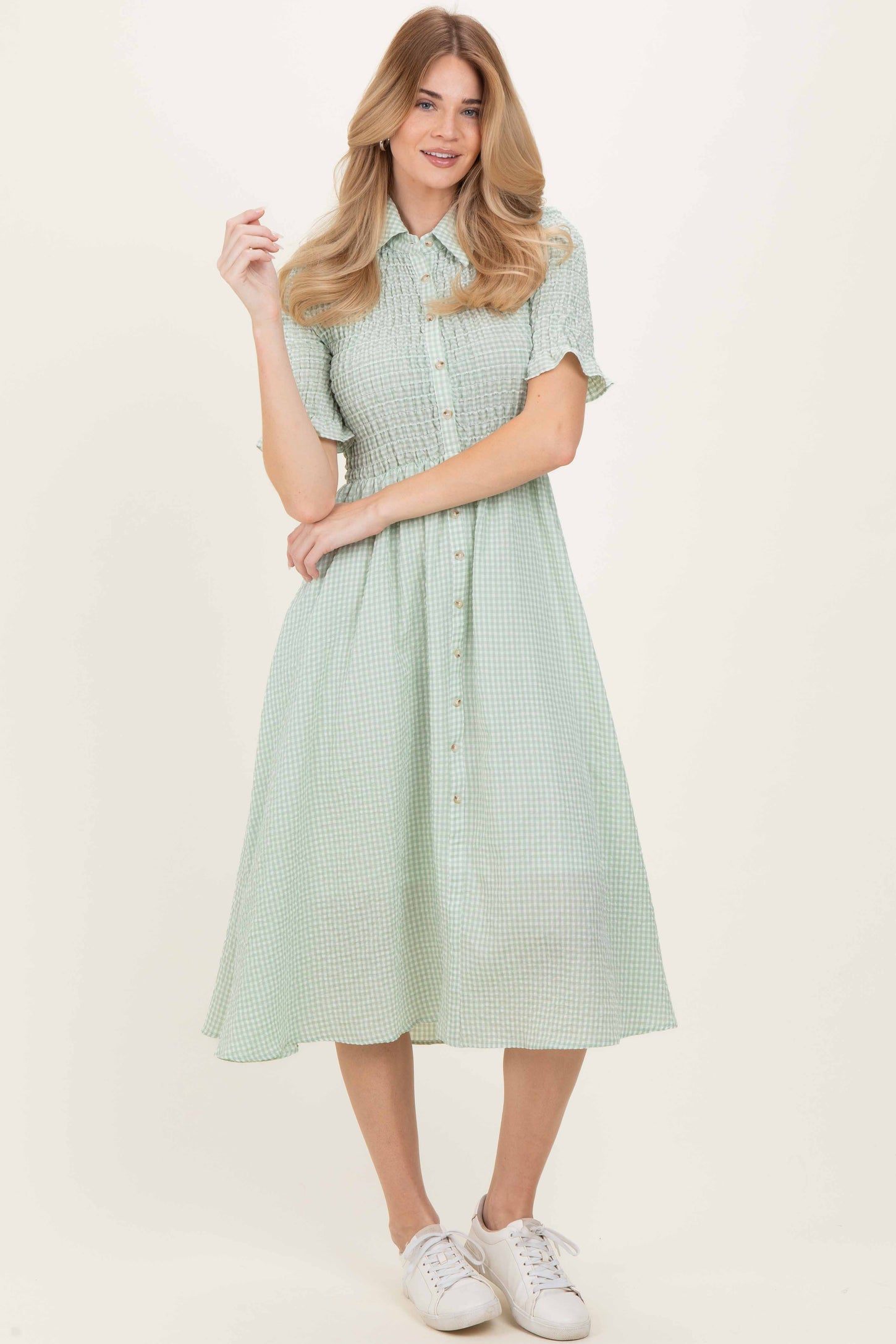 woman wearing a green checkered button-up dress with short sleeves and a flared skirt, standing in white sneakers