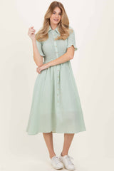 woman wearing a green checkered button-up dress with short sleeves and a flared skirt, standing in white sneakers