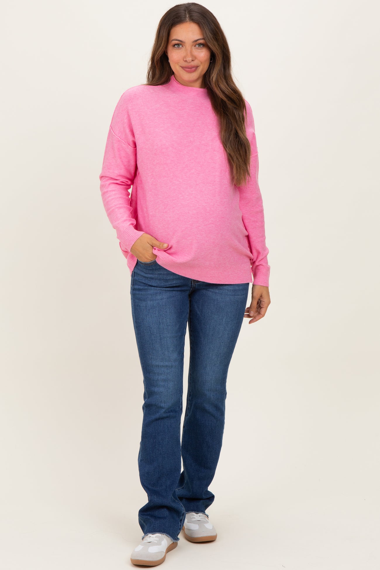 woman wearing a bright pink maternity sweatshirt and blue jeans, showcasing her baby bump