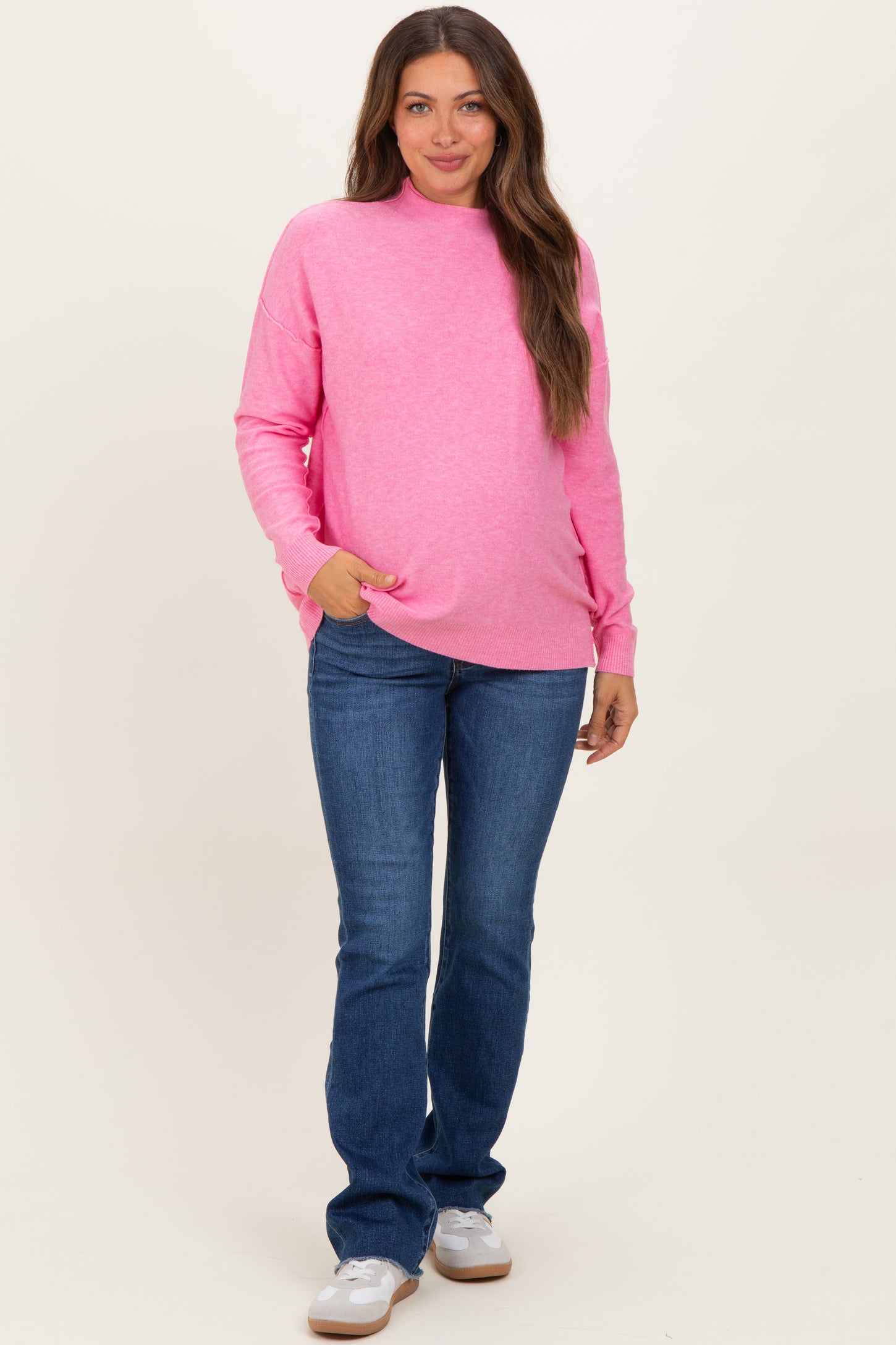 woman wearing a bright pink maternity sweatshirt and blue jeans, showcasing her baby bump