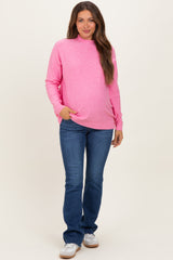 woman wearing a bright pink maternity sweatshirt and blue jeans, showcasing her baby bump
