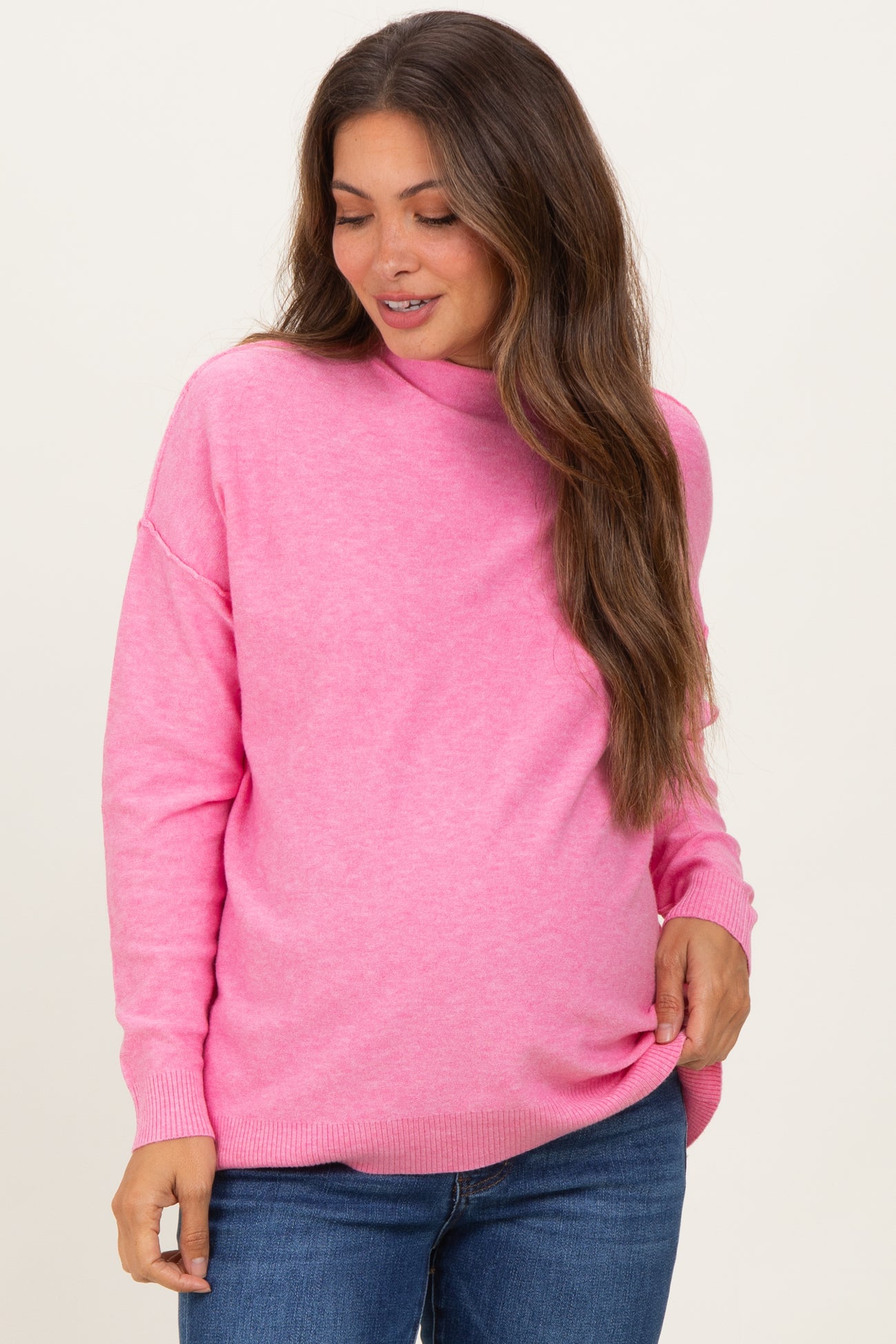 woman wearing a pink maternity sweater with a relaxed fit and long sleeves, showing her baby bump
