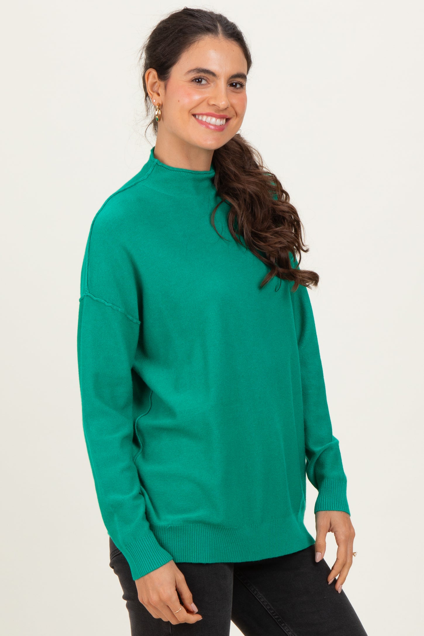 woman wearing a green oversized sweater with a high neckline and long sleeves, smiling against a light background