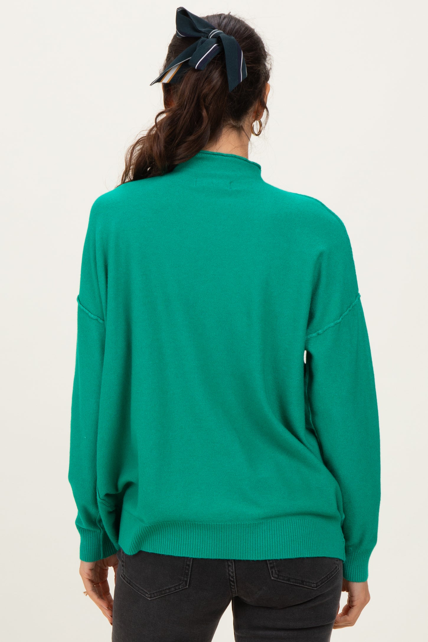 woman wearing a green oversized sweater with a high neckline and drop shoulders, viewed from the back