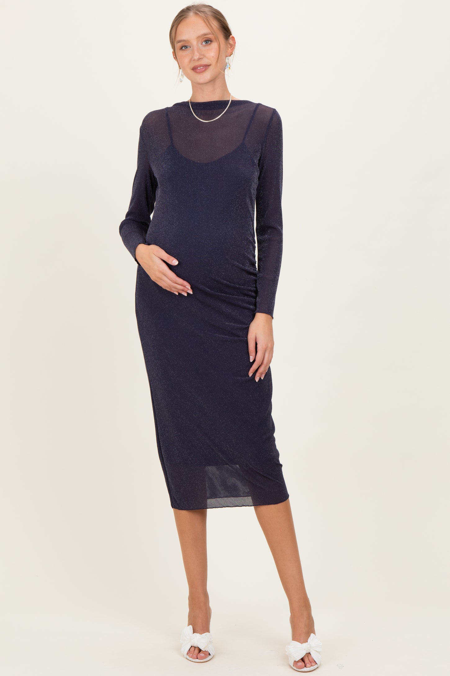woman wearing a navy blue long sleeve maternity dress with shimmer detail, gently holding her baby bump