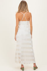 woman wearing a cream striped maternity maxi dress with a crisscross back and flowing fabric