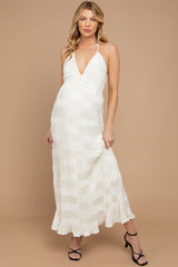 woman wearing a white striped maternity maxi dress with a halter neck, showing her baby bump