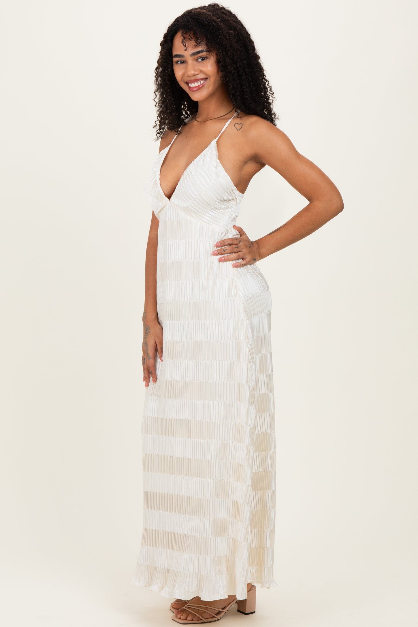 woman wearing a white maxi dress with a deep V-neck and a pleated design, standing and smiling