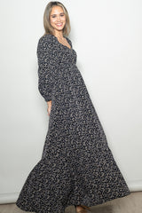 woman wearing a black floral maxi dress with long sleeves and a fitted bodice, smiling against a neutral background