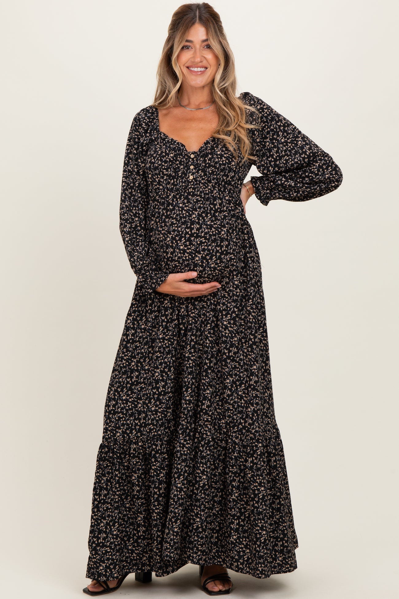 woman wearing a black floral maternity maxi dress and holding her baby bump