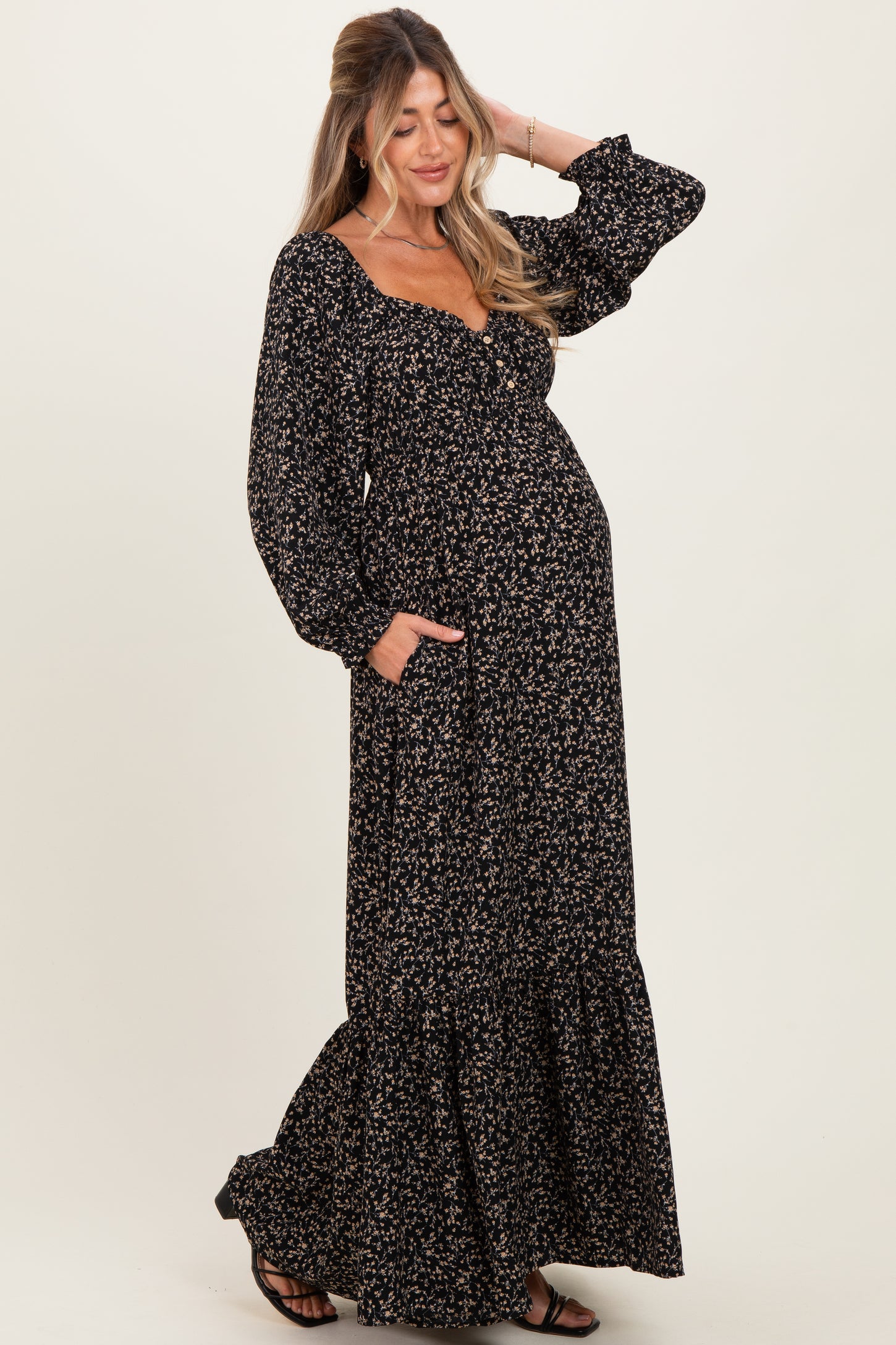 woman wearing a black floral maternity maxi dress with long sleeves and pockets, showing her baby bump