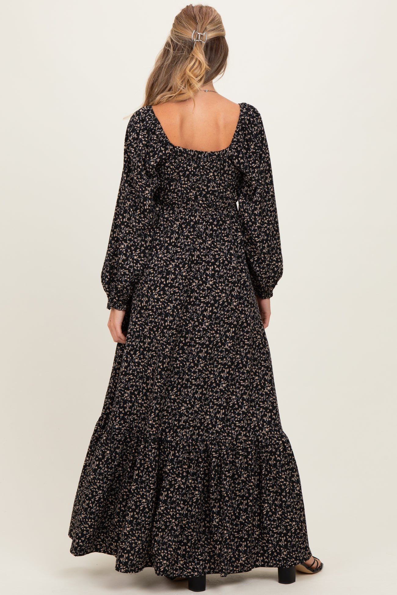 woman wearing a black floral maternity maxi dress with puff sleeves and a tiered skirt, viewed from the back