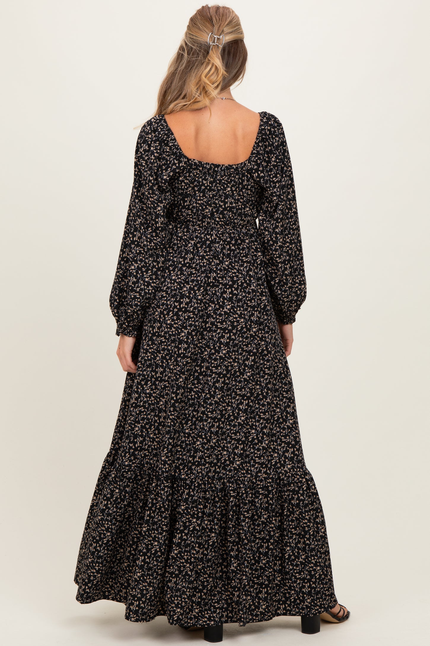 woman wearing a black floral maternity maxi dress with puff sleeves and a tiered skirt, viewed from the back