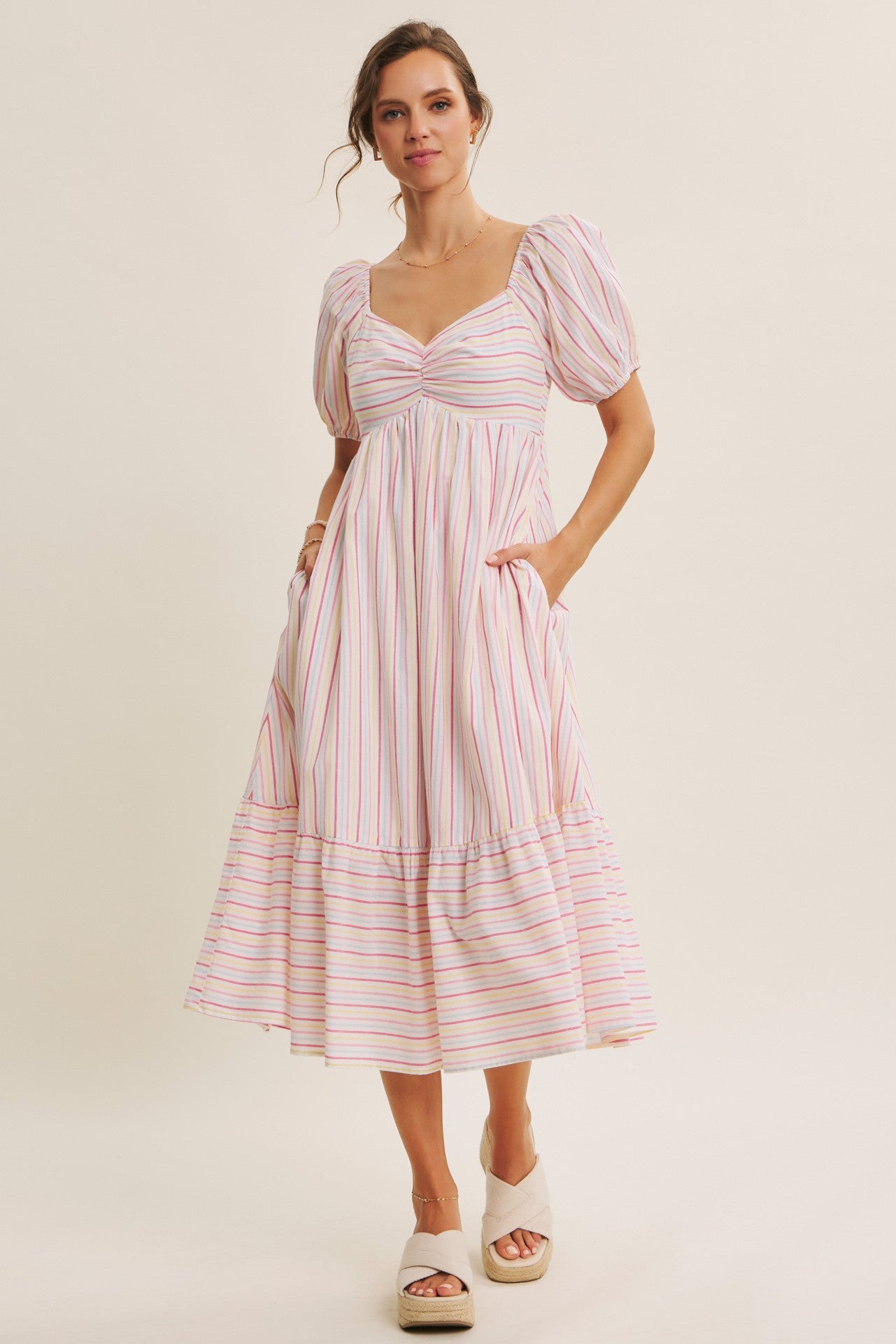 woman wearing a striped midi dress with puff sleeves and pockets, styled with beige platform sandals