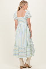 woman wearing a light blue striped puff sleeve maxi dress with a tiered hem and back details, facing away from the camera