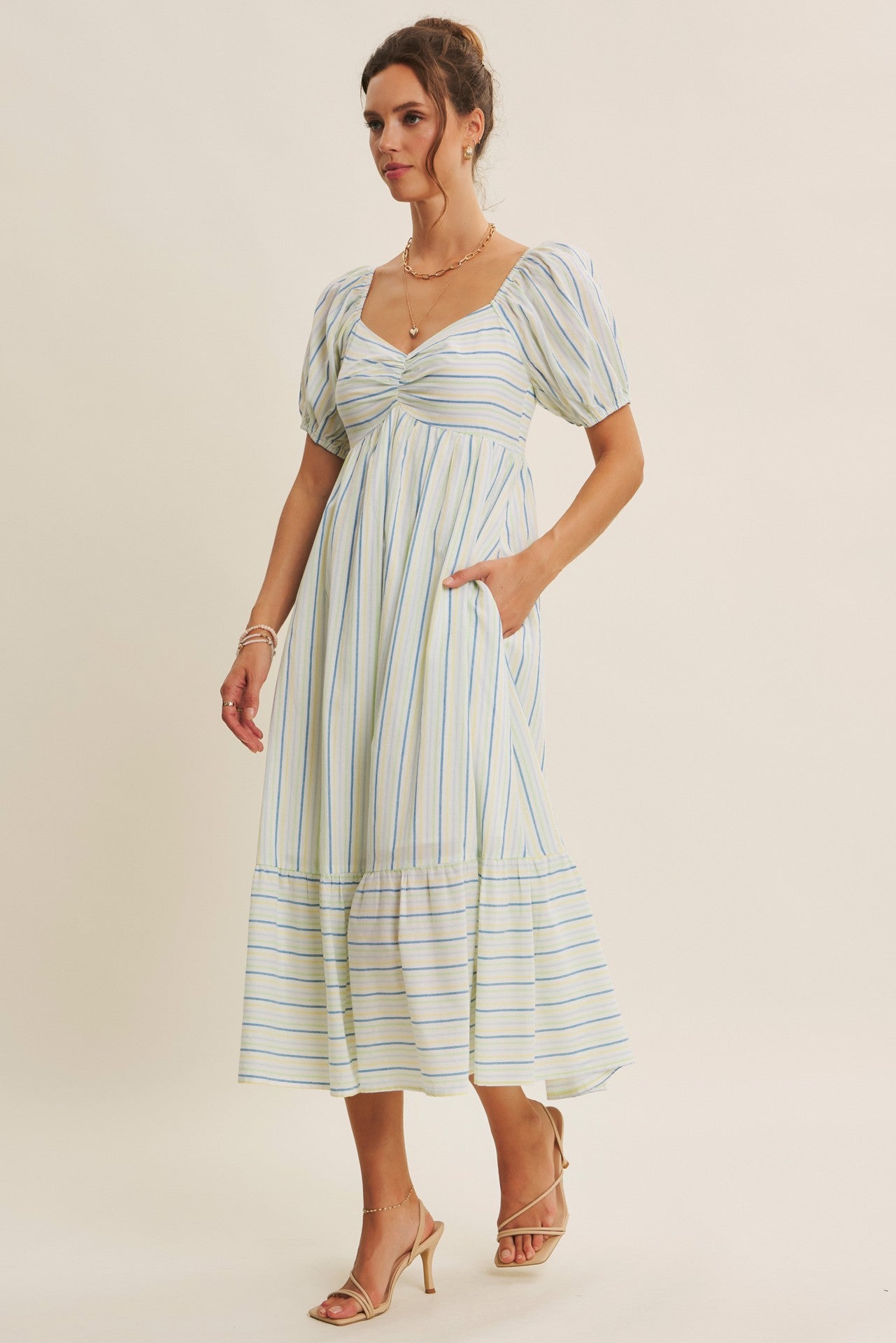 woman wearing a striped midi dress with puff sleeves and pockets, styled with strappy heels