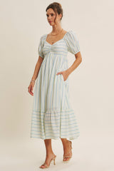 woman wearing a striped midi dress with puff sleeves and pockets, styled with strappy heels