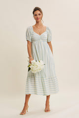 woman wearing a white striped midi dress with puff sleeves and a square neckline, holding a bouquet of flowers
