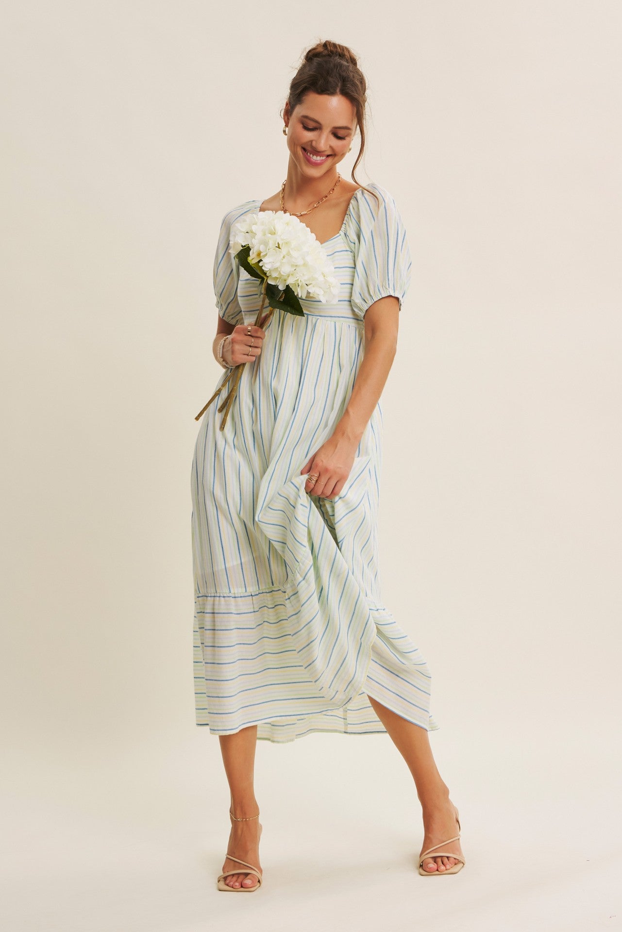 woman wearing a light blue and white striped midi dress with puff sleeves, holding white flowers and smiling