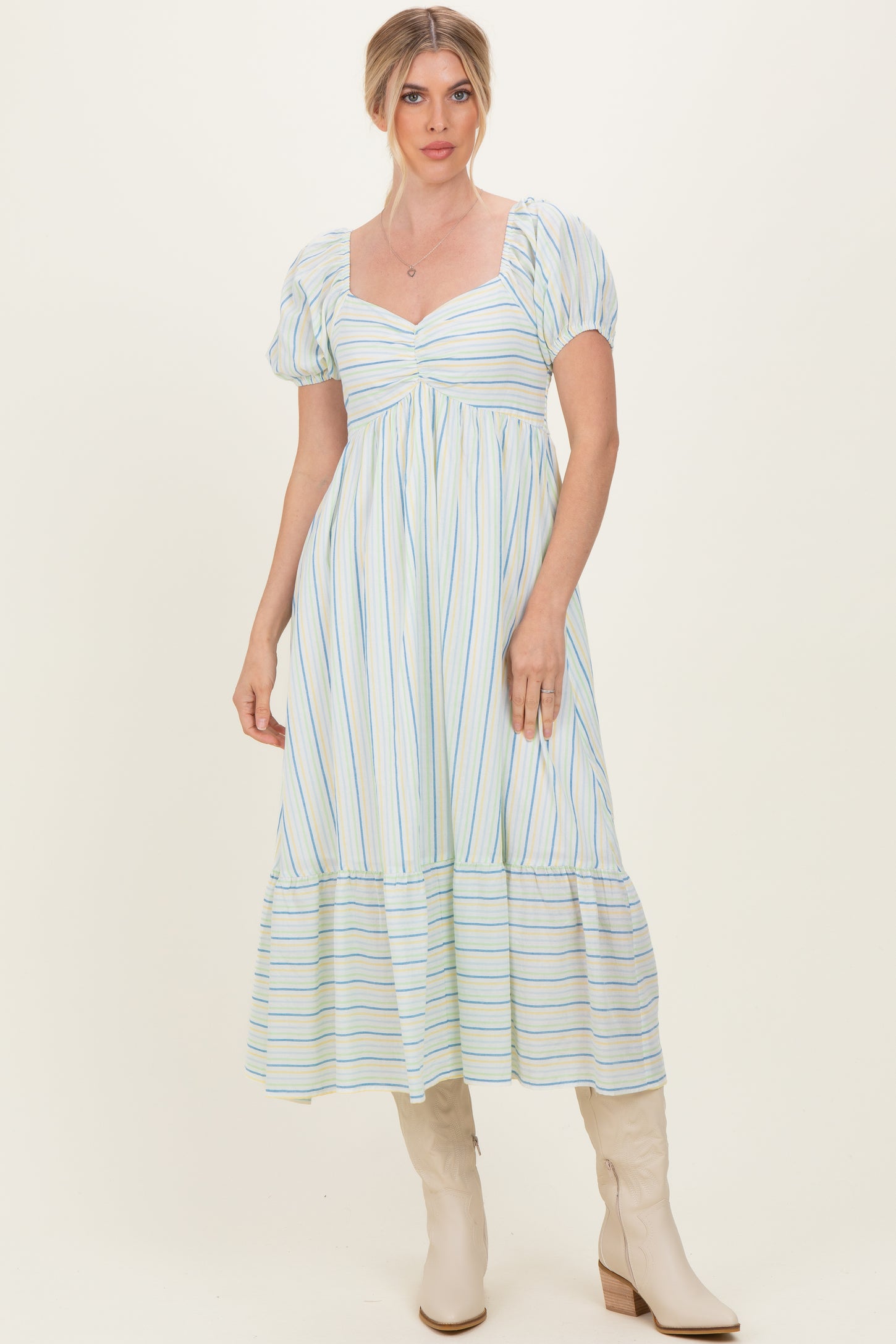 woman wearing a light blue and white striped puff sleeve maxi dress with a tiered skirt and beige knee-high boots