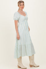 woman wearing a blue and white striped maxi dress with puff sleeves and a tiered hem, standing in a neutral background
