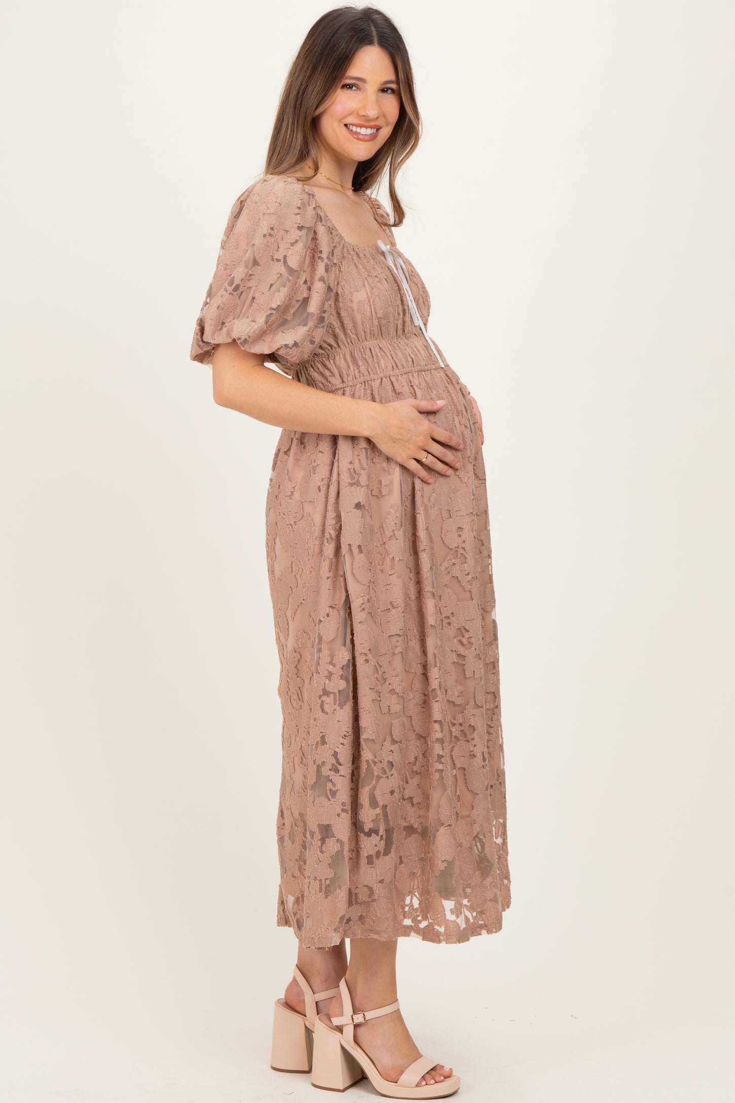 woman wearing a beige lace maternity dress and holding her baby bump