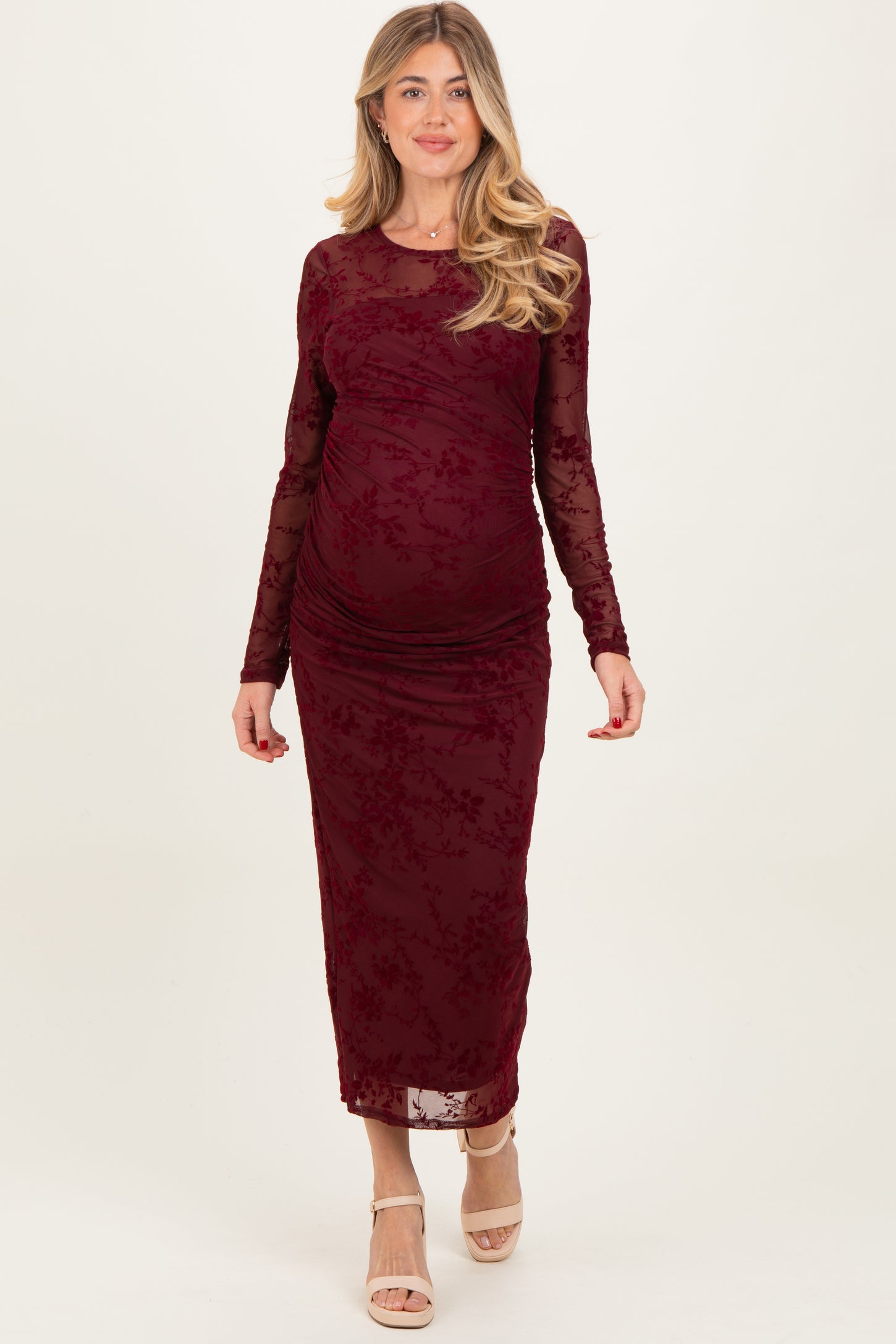 woman wearing a burgundy long sleeve maternity dress with floral lace overlay and a visible baby bump