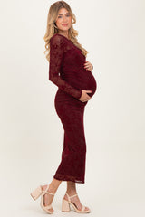 woman wearing a burgundy long sleeve velvet maternity dress and holding her baby bump