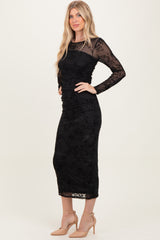 woman wearing a black floral lace long sleeve midi dress with a fitted silhouette and a sheer neckline