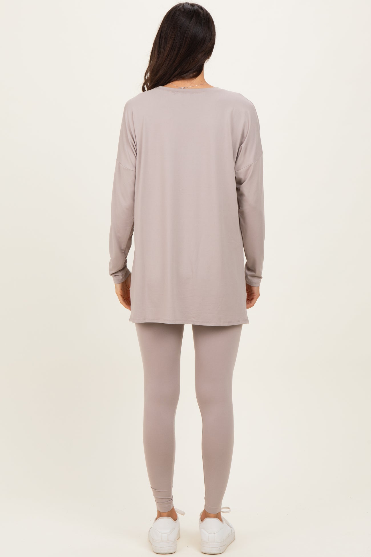 woman wearing a long sleeve taupe tunic top and matching leggings, paired with white sneakers, standing with back to the camera
