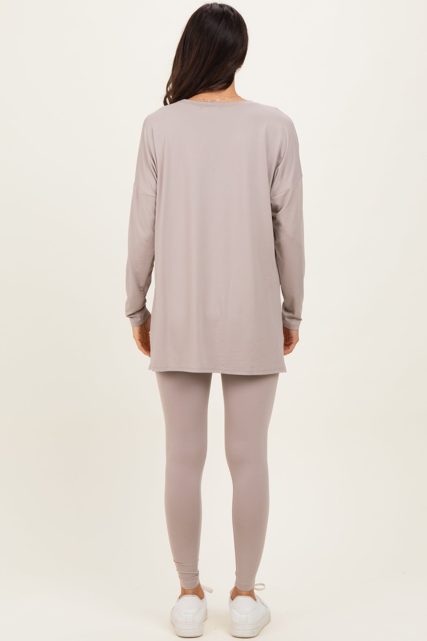 woman wearing a long sleeve taupe tunic top and matching leggings, paired with white sneakers, standing with back to the camera