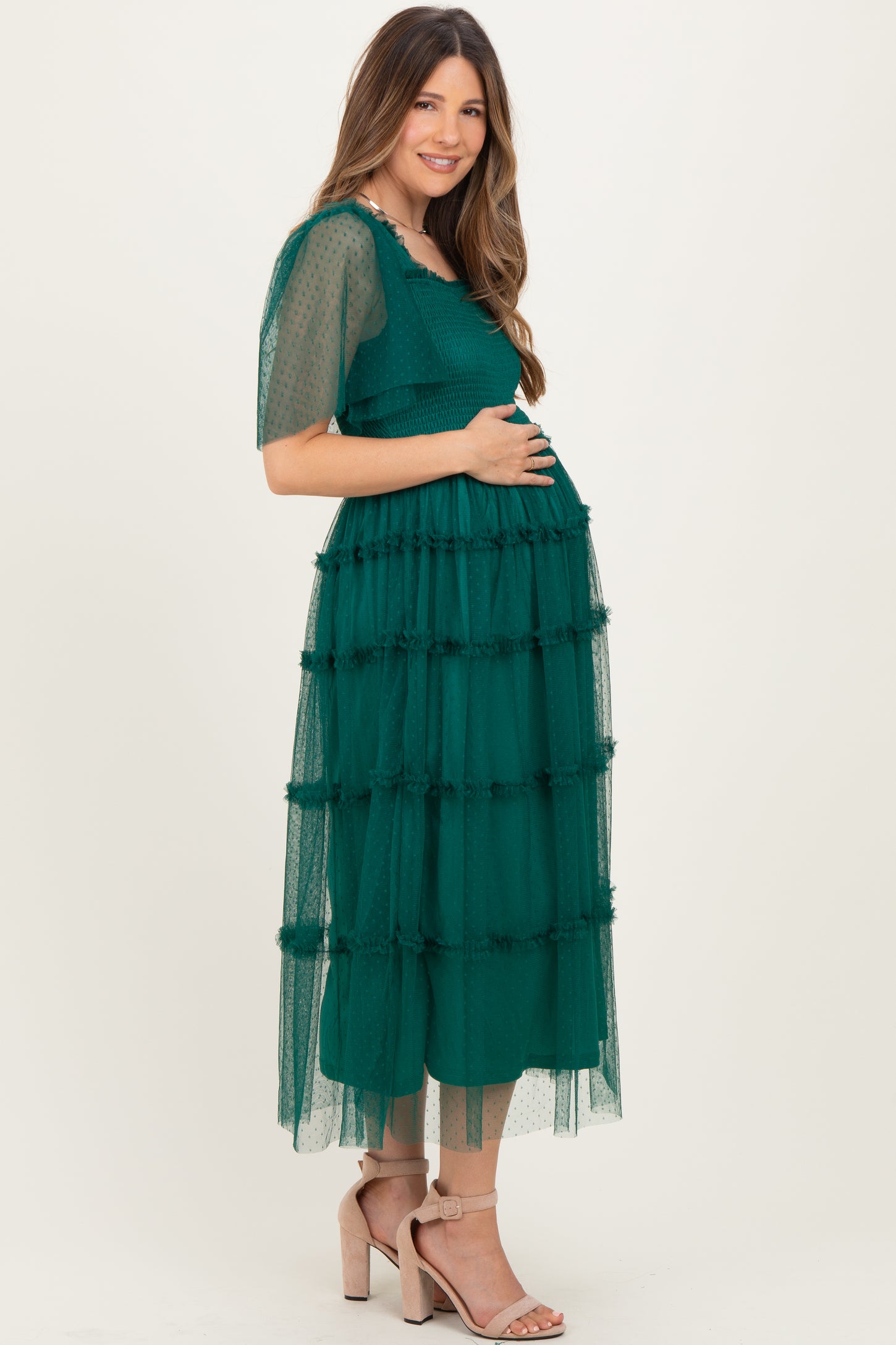 woman wearing a green tiered maternity dress with short sleeves and holding her baby bump