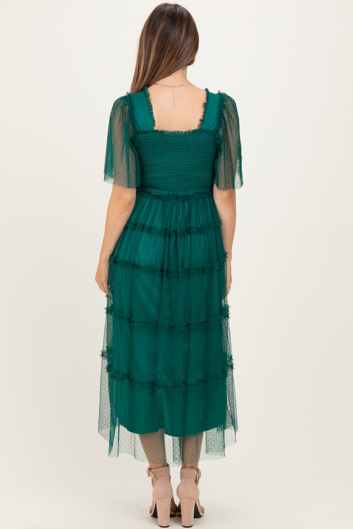 woman wearing a dark green maternity dress with tiered layers and sheer puff sleeves, showcasing a stylish back view
