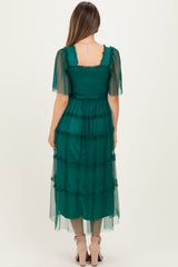 woman wearing a dark green maternity dress with tiered layers and sheer puff sleeves, showcasing a stylish back view
