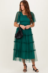 woman wearing a dark green tiered tulle midi dress with short sleeves and a square neckline, holding a black bag